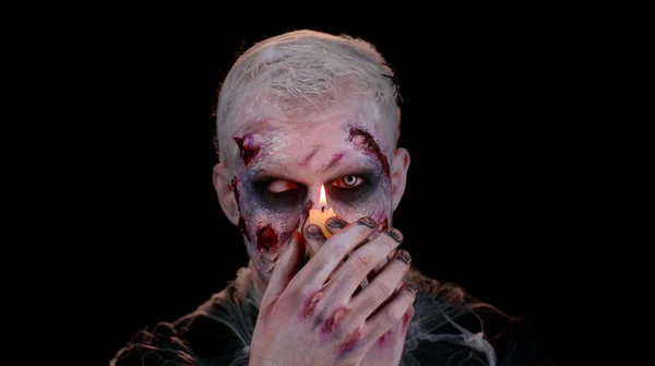 Man with Halloween zombie bloody wounded makeup, trying to scare, spells conjures over a candle — Stock Photo, Image