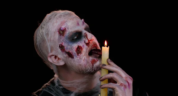 Man alone with Halloween zombie bloody wounded makeup, trying to scare spells conjures over a candle — Stock Photo, Image