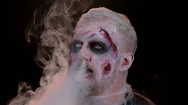 Homem assustador cicatrizes sangrentas feridas assustadoras rosto Halloween cara morto-vivo sopra fumaça do nariz, sorrisos — Fotografia de Stock