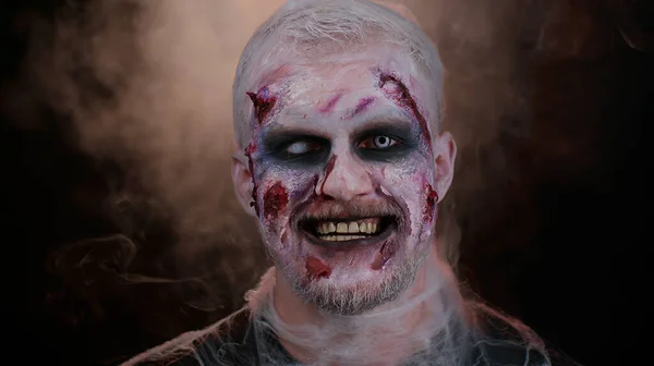 Straszny ranny zombie Halloween nieumarły potwór człowiek robi miny, patrzy w kamerę i uśmiecha się strasznie — Zdjęcie stockowe