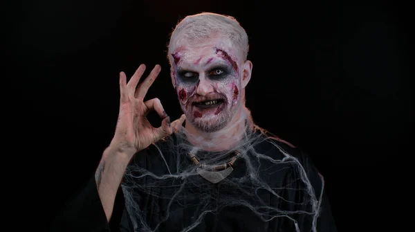 Creepy man Halloween zombie showing Ok gesture, like sign positive something good, smiles terribly