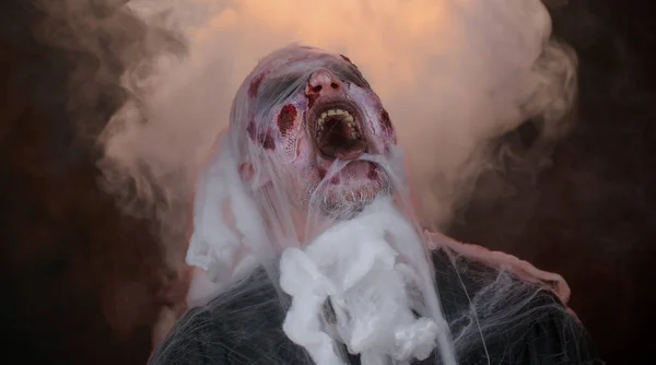 Sinistro uomo orribile spaventoso zombie di Halloween guardando minaccioso alla fotocamera soffia fumo dal naso, dalla bocca — Foto Stock