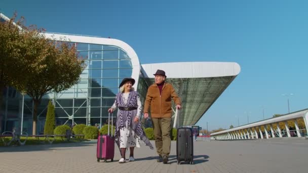 Stílusos nyugdíjas család pár nagyi nagypapa séta bőrönd táskák a repülőtér csarnokában — Stock videók