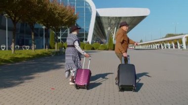 Mutlu büyükanne büyükbaba valizlerle havaalanı salonuna yürüyor, dansı kutlayalım.