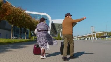 Neşeli büyükbaba valizlerle havaalanı salonuna yürüyor, dansı kutluyor.