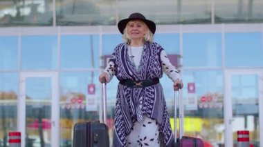 Yaşlı emekli turist büyükanne iş kadını havaalanı kapısından bavul çantasıyla geliyor.