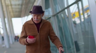 Büyük turist büyükbaba uluslararası havaalanında yürüyor, cep telefonu kullanıyor, mesajlaşıyor.