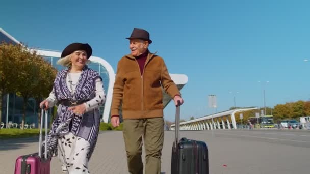 Elderly husband wife retirees tourists go to airport terminal for boarding with luggage on wheels — Stock Video