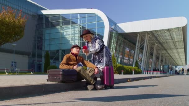 Senior penzisté turisté babička dědeček čeká na nástupu v blízkosti mezinárodní letištní haly — Stock video
