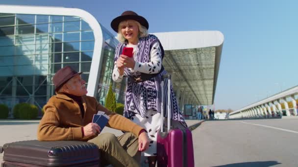 Senior pensioner tourists grandmother grandfather buy tickets online on mobile phone near airport — Stock Video