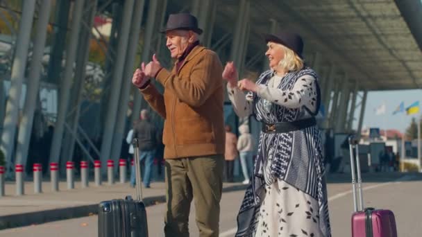 Idős férj feleség nyugdíjasok turisták megy a repülőtér terminál beszállás poggyász kerekeken — Stock videók