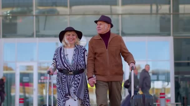 Stílusos nyugdíjas család nagypapa séta bőrönd táskák a repülőtér csarnokában — Stock videók