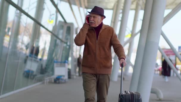 Senior toeristische grootvader lopen op de internationale luchthaven hal, met behulp van mobiele telefoon, praten — Stockvideo
