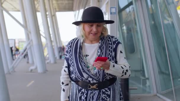在国际机场大厅里散步、使用手机、发短信的高级旅游祖母 — 图库视频影像