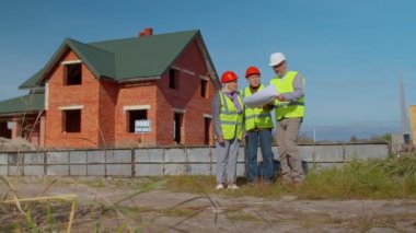 İnşaat binasının planlarıyla proje çalışmalarını tartışan kıdemli inşaat mühendisleriyle mimar.