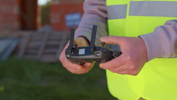 Operador de drones segurando controlador remoto controla uma aeronave na frente do canteiro de obras — Vídeo de Stock