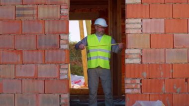 Mühendis mimar evin inşaat alanında mezurayla ölçüm yapıyor.