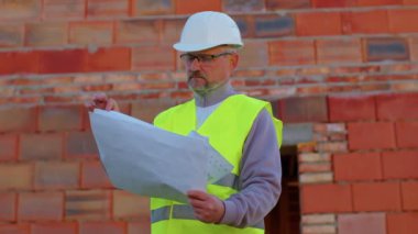 İşçi tasarımcı mimar ev ve emlak şantiyesinin planlarını analiz ediyor.