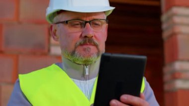İnşaat alanında dijital tablet bilgisayarı olan mimar bina planlarını analiz ediyor.