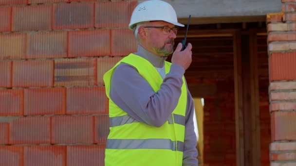 Arquitecto ingeniero constructor operar con radio hablando para controlar el trabajo en el sitio de la casa de construcción — Vídeo de stock