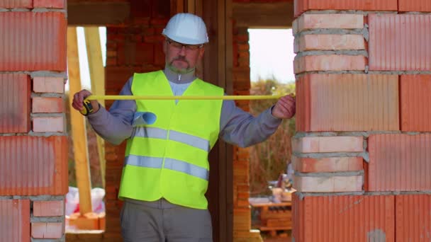 Építőmérnök építész szakember méréseket végez egy mérőszalaggal az építkezésen — Stock videók