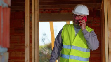 İnşaat alanında çalışmayı kontrol etmek için cep telefonuyla konuşan profesyonel mimar.