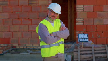 İnşaat mühendisi inşaat alanında uzman kamera ve arka plandaki eve bakıyor.