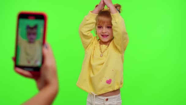 Veselý legrační malé teen dívka dítě tančí na kameře natáčení videa pomocí telefonu na zdi chroma klíč — Stock video