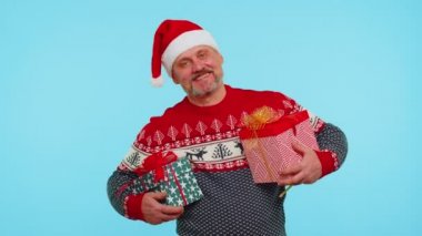 Noel Baba süveter giyen neşeli adam iki Noel hediyesi kutusu sunuyor, ellerini kameraya uzatıyor.
