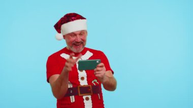 Yeni yıl tişörtlü ve şapkalı endişeli adam cep telefonuyla yarış oyunları oynuyor.