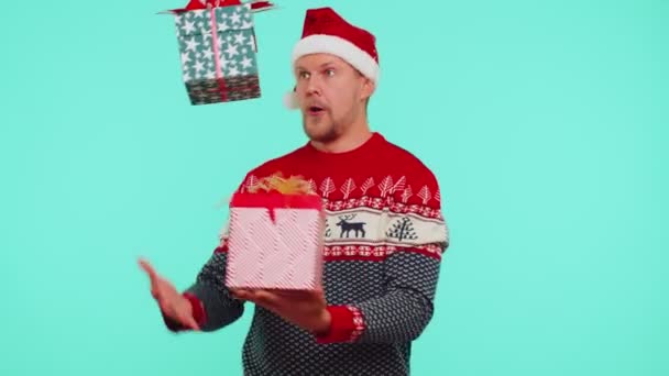 Hombre lleva rojo Año Nuevo presentando cajas de regalo de Navidad, extiende sus manos a la cámara sonriendo — Vídeos de Stock