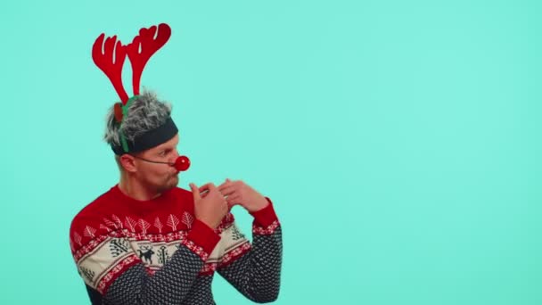 Adam kırmızı yeni yıl kazak geyiği giyer ve boş reklam alanına işaret eder. — Stok video