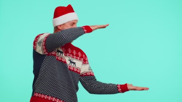 Man draagt rood Nieuwjaar trui hert tonen duimen omhoog en wijzen naar op lege advertentieruimte — Stockvideo