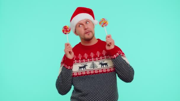 Zabawny mężczyzna w czerwonym swetrze noworocznym, kapelusz z lizakami w paski, taniec, robienie głupich min — Wideo stockowe