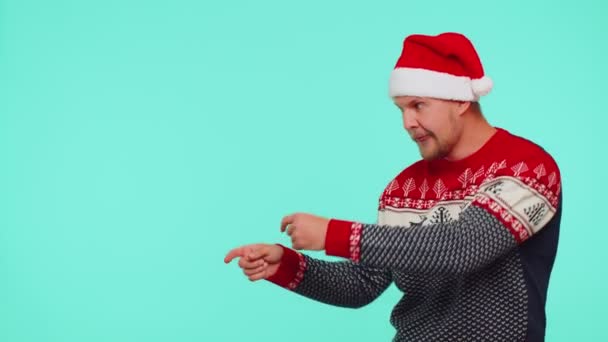 Seorang pria mengenakan sweater merah Tahun Baru rusa menunjukkan jempol ke atas dan menunjuk pada ruang iklan kosong — Stok Video