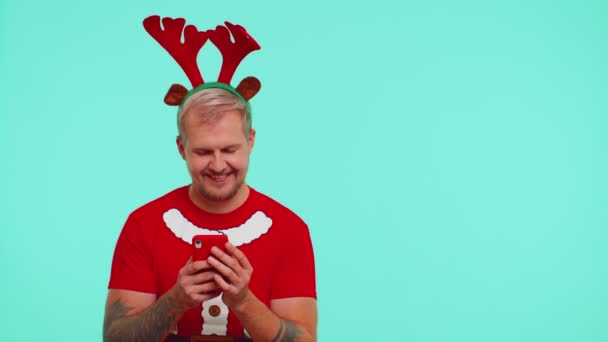 Man i t-shirt Santa Christmas med mobiltelefon visar pekar tom plats, annonsområde — Stockvideo