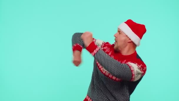 Fiatal felnőtt férfi pulóverben Mikulás karácsonyi kalap ugrik alulról tánc bolondozás körül szórakozás — Stock videók