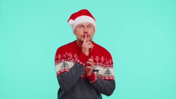 Mann trägt roten Weihnachtspulli drückt Zeigefinger an Lippen macht Schweigegegeste — Stockvideo