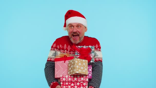 Homem de camisola vermelha de Natal, chapéu de Papai Noel, sorrindo, segurando muitas caixas de presente — Vídeo de Stock