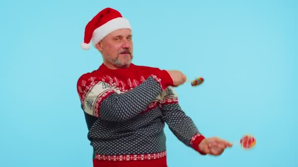 Joyful man in red Christmas sweater, hat holding candy striped lollipops, dancing making silly faces — Stock Video