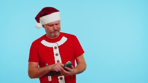 穿着圣诞T恤，戴着帽子的男人用手机在网上打印新的帖子，在网上购物，浏览 — 图库视频影像