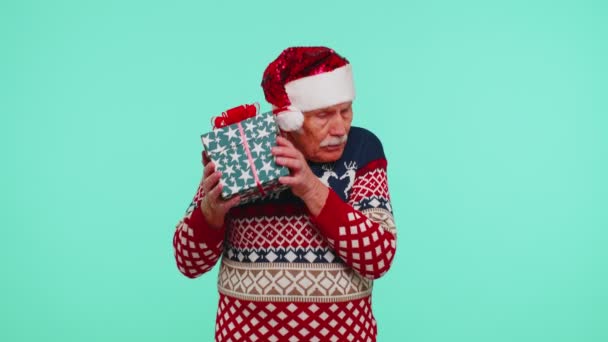 Старший дедушка в рождественском свитере получил подарок, заинтересованный в том, что внутри подарочной коробки — стоковое видео