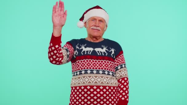 Grandfather man in Christmas sweater with deers waves hand palm in hello gesture welcomes someone — Stock Video