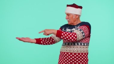 Noel Baba süveteri giyen büyükbaba başparmaklarını gösterip boş yeri işaret ediyor, reklam alanı.