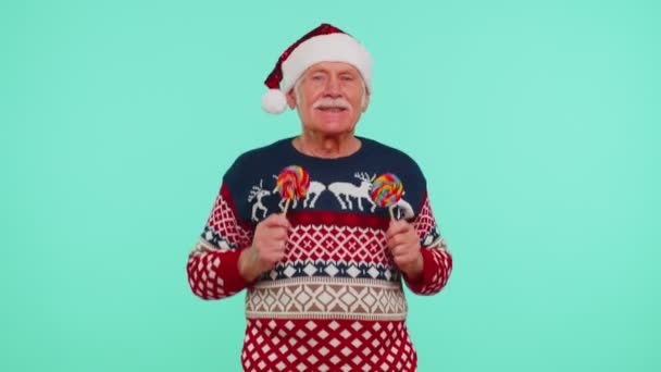Ανώτερος παππούς σε χριστουγεννιάτικο πουλόβερ κρατώντας καραμέλα ριγέ γλειφιτζούρια, χορό κάνοντας ανόητα πρόσωπα — Αρχείο Βίντεο