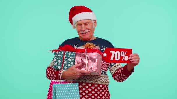 Starší muž ve vánočním svetru ukazuje dárkové krabice a 70 Procento sleva nápisy banner text — Stock video