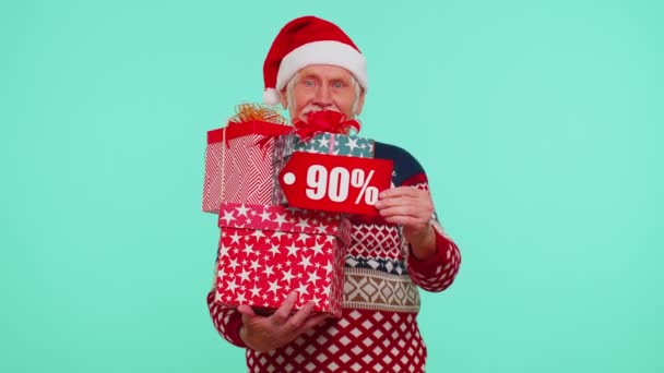 Senior muž ve vánočním svetru ukazuje dárkové krabice a 90 procent sleva nápisy banner text — Stock video
