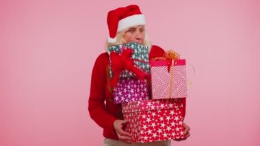 Noel süveteri giymiş yaşlı bir büyükanne elinde bir sürü hediye kutusu tutuyor.