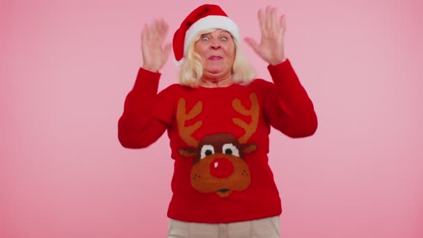 Бабушка в рождественском свитере с оленями волнами ладонью в привет жест приветствует кого-то — стоковое видео