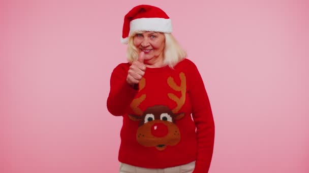 Бабушка носит красный новогодний свитер с оленями поднимает большие пальцы вверх согласуется с чем-то хорошим, например — стоковое видео